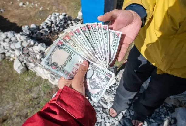 A traveller's hands holding a fanned stack of Nepalese rupee banknotes.