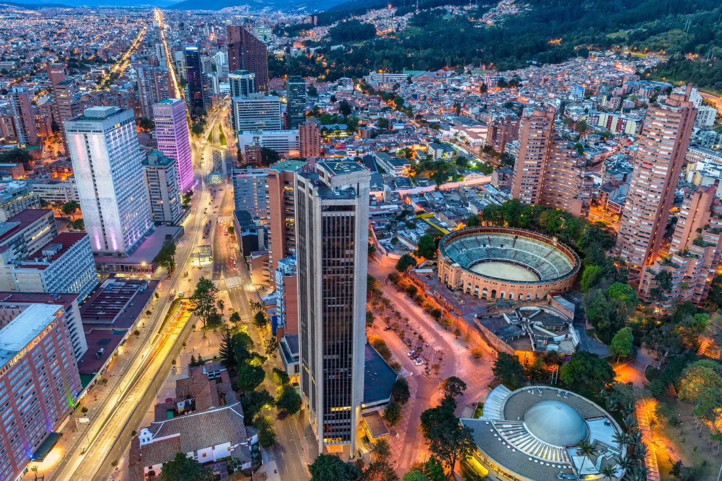 Aerial night view of a Colombian city skyline with an illuminated stadium