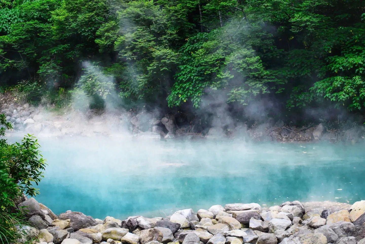 Turquoise hot spring pool surrounded by rocks and forest in Beitou