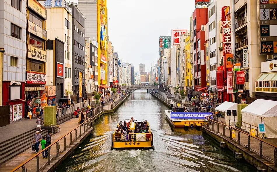 Tourist boat travelling along the Dotonbori canal surrounded by shops and neon signs in Osaka