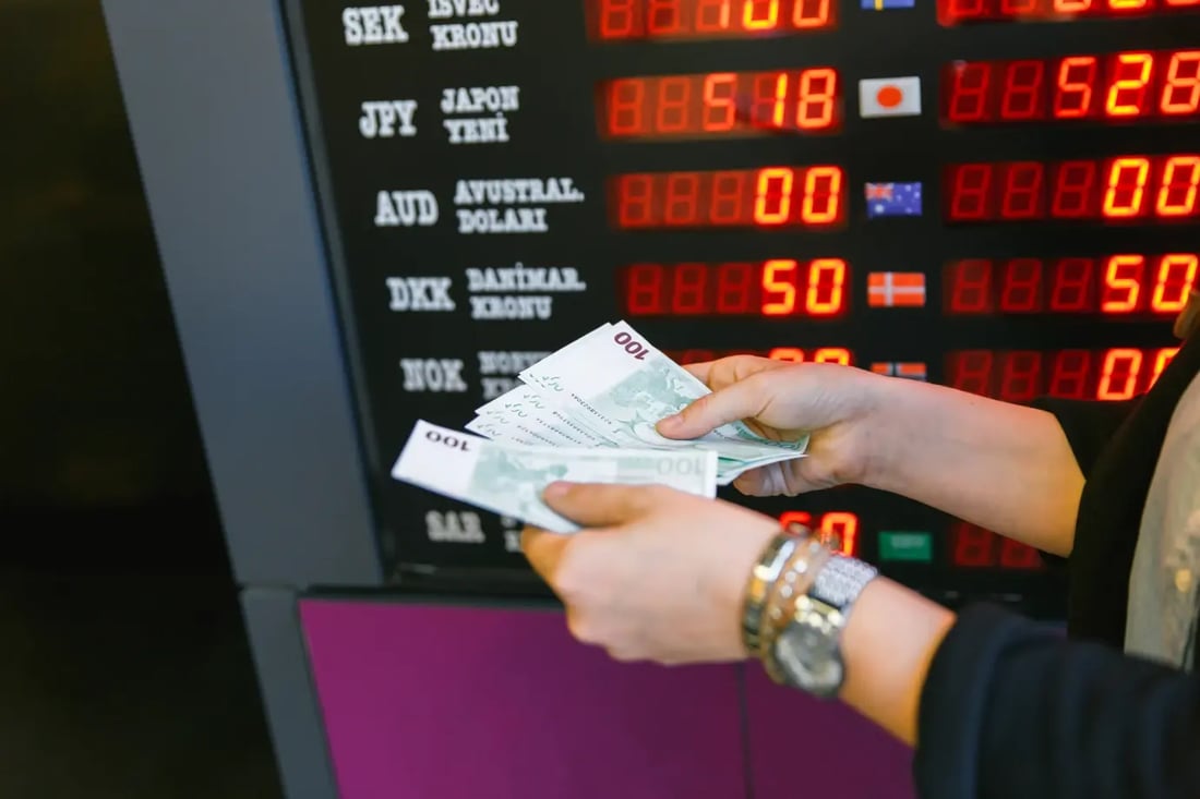 Customer holding foreign currency in front of Crown Currency exchange rate board.