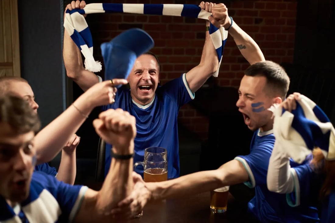 Excited sports fans cheering for the Commonwealth Games, in a Glasgow bar with drinks