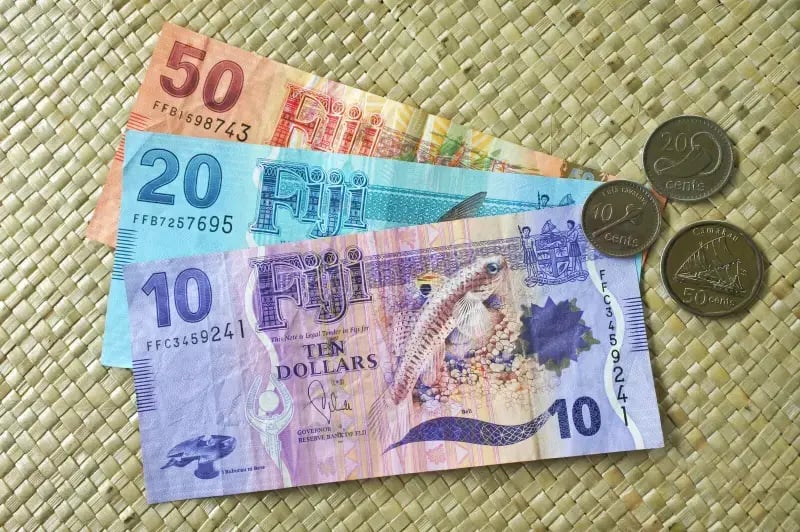 Fijian currency featuring 50, 20, and 10 dollar banknotes alongside coins on a woven mat background.