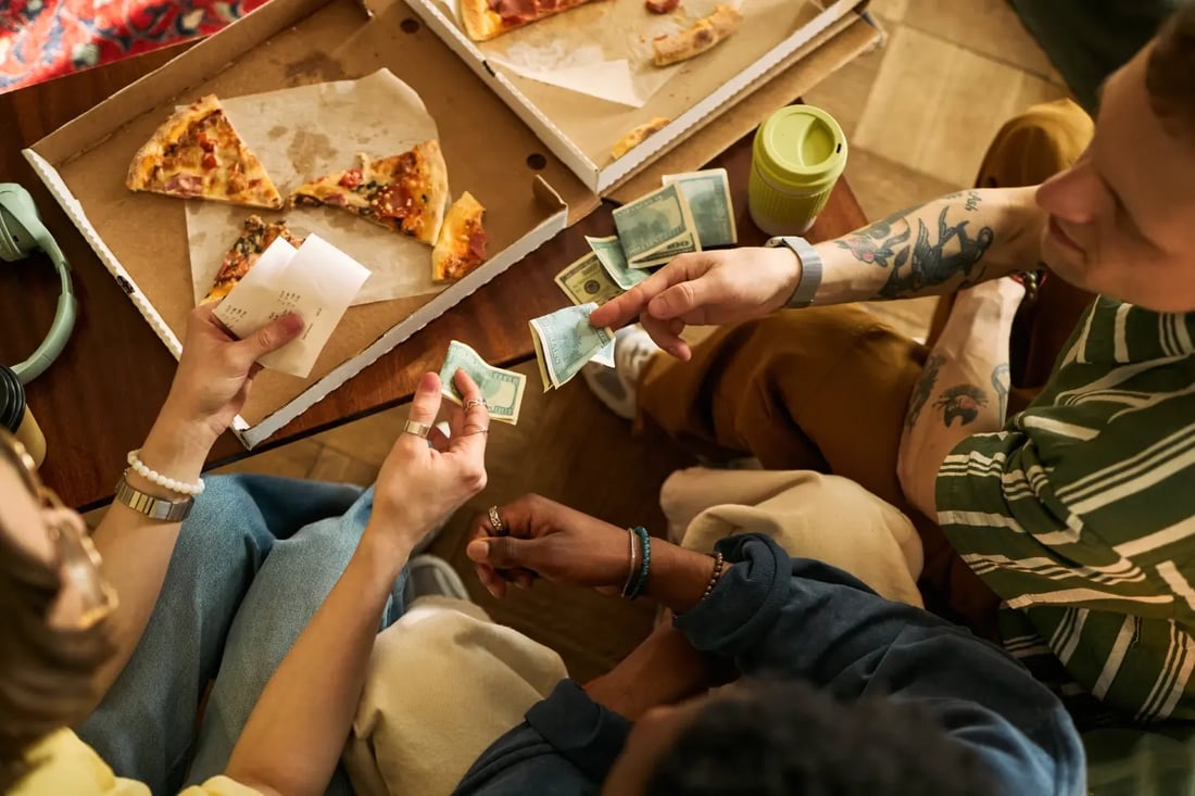 Friends counting cash to split travel costs over pizza