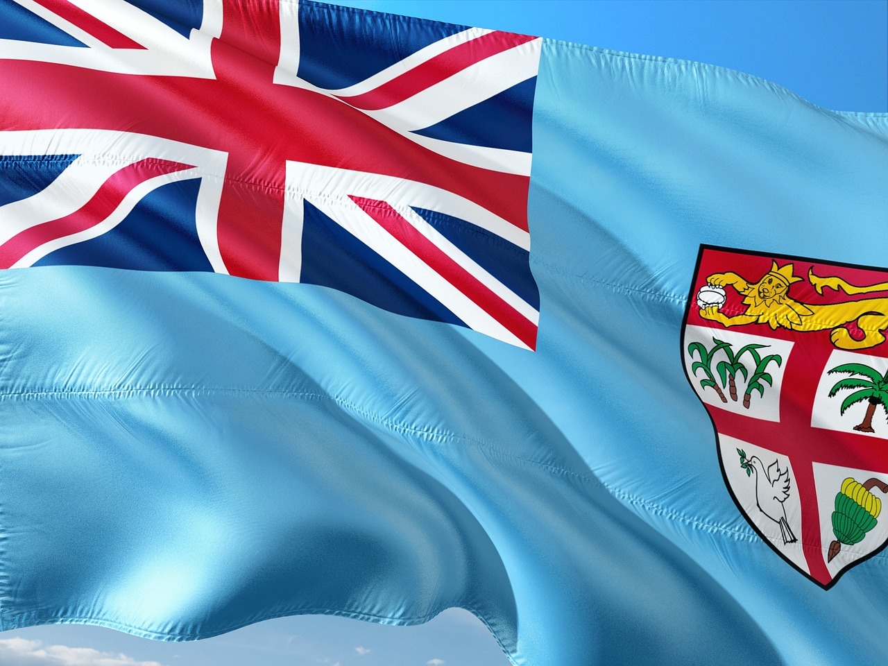 Flag of Fiji waving against a clear blue sky, featuring the Union Jack and Fiji’s national shield emblem.