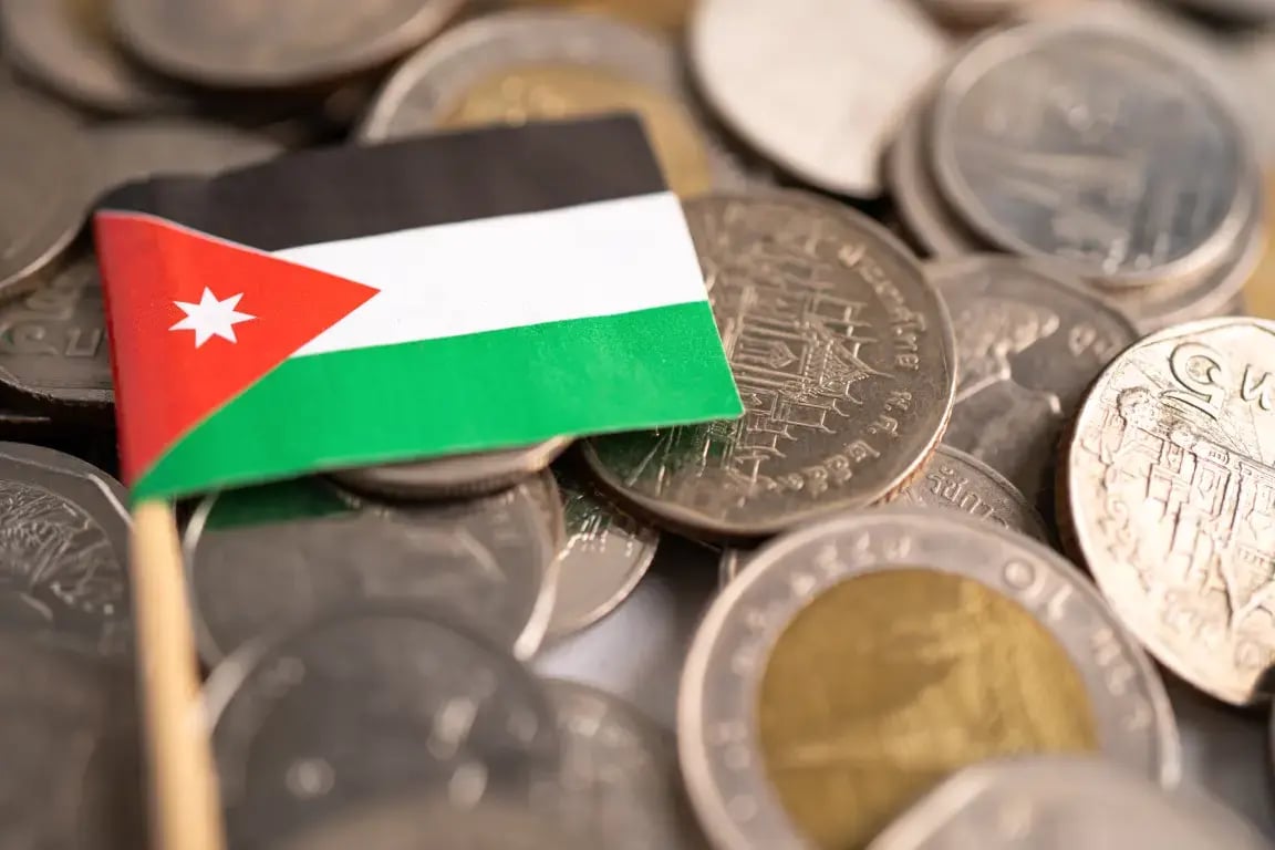 Small Jordanian flag standing upright among a pile of dinar coins