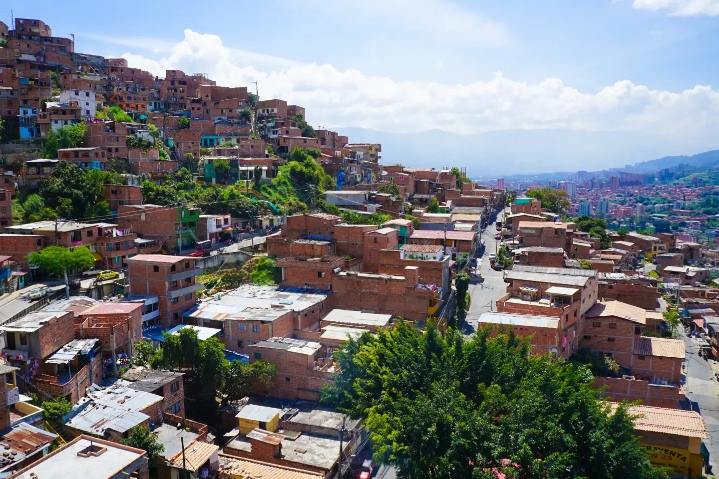 Aerial view of hillside houses in Comuna 13, Medellín, with the city skyline behind