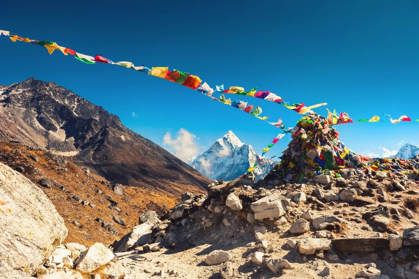 Prayer flags strung across a rocky ridge with a snow-capped Himalayan peak behind, Everest Base Camp trail, Nepal.