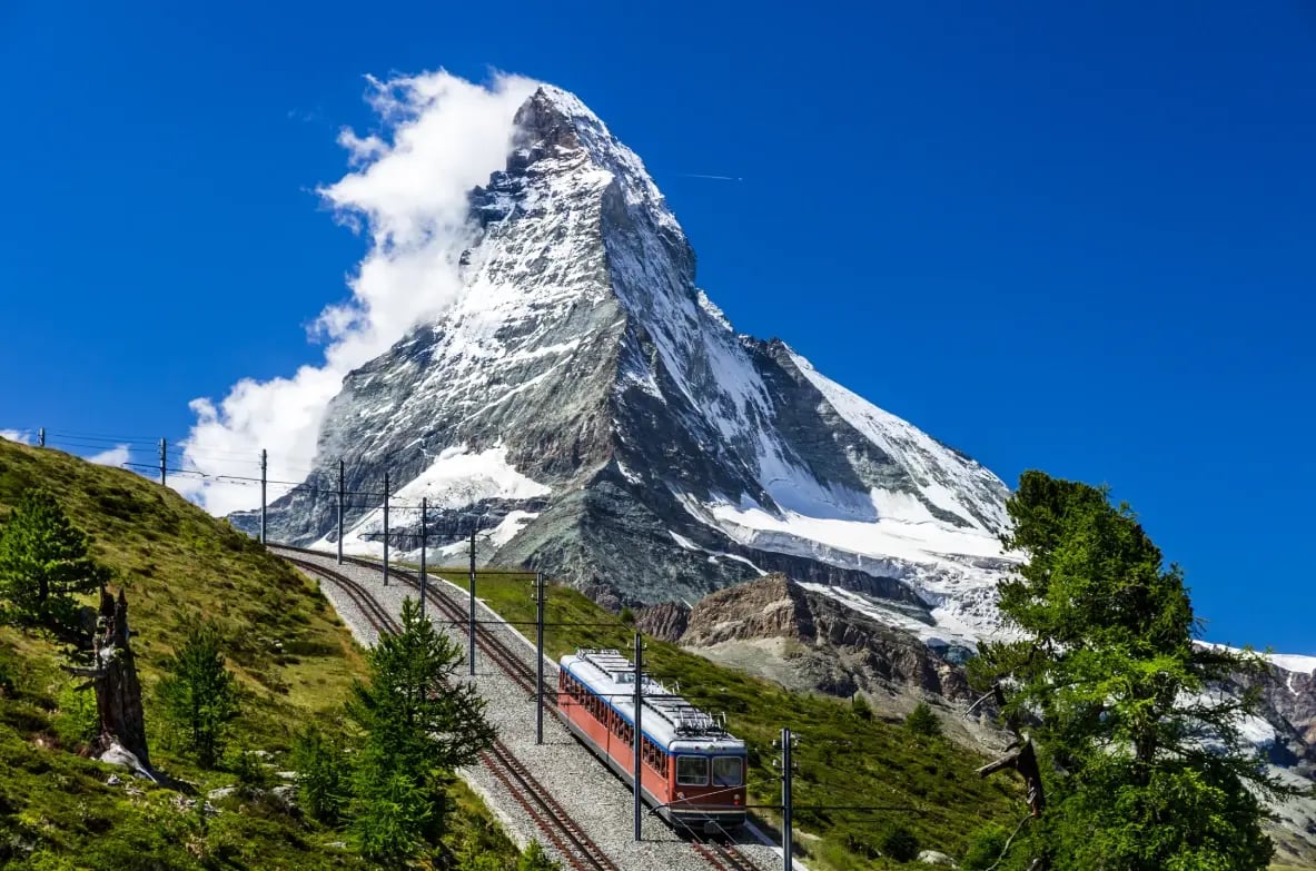 The Matterhorn rising above Zermatt, with the red Gornergrat Bahn mountain railway in the foreground, Switzerland.