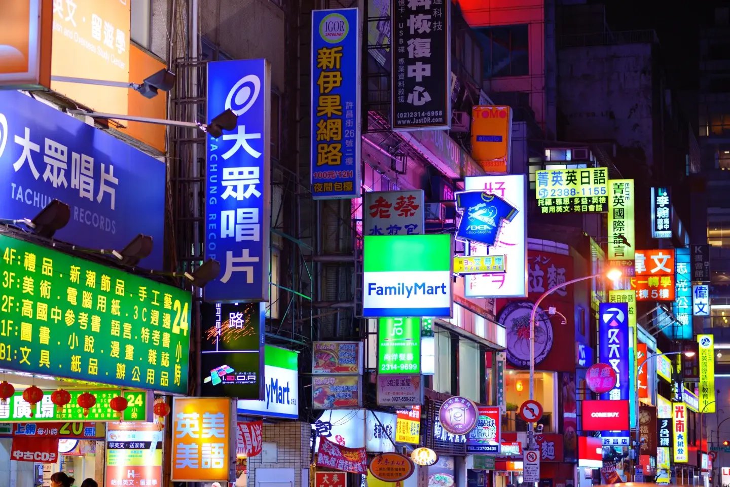 Neon shop signs, including a FamilyMart storefront, on a Taipei street after dark