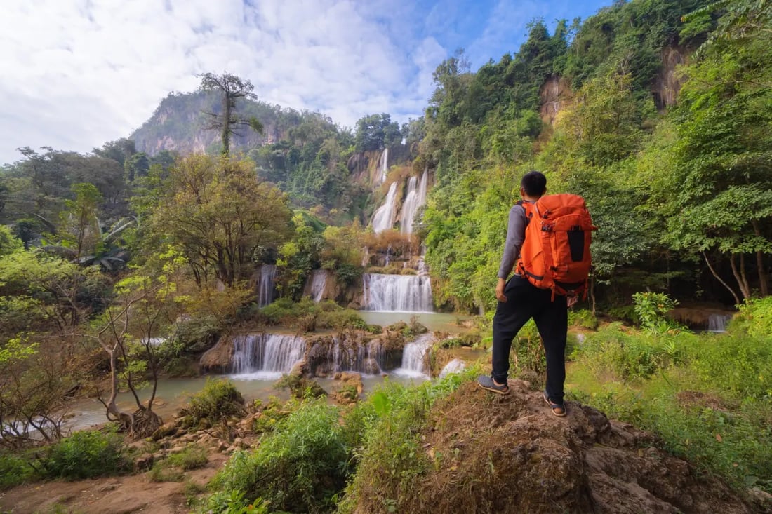 Solo backpacker overlooking a tiered jungle waterfall in Southeast Asia