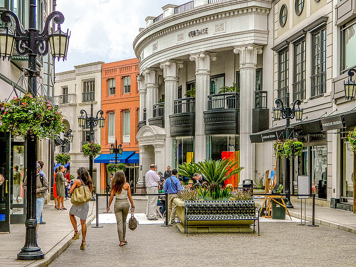 Shoppers walking along Rodeo Drive in Beverly Hills with luxury stores and palm-lined streets.