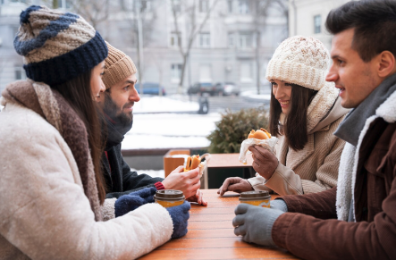 Group of people sitting at an outdoor café in winter, eating and drinking in a European city