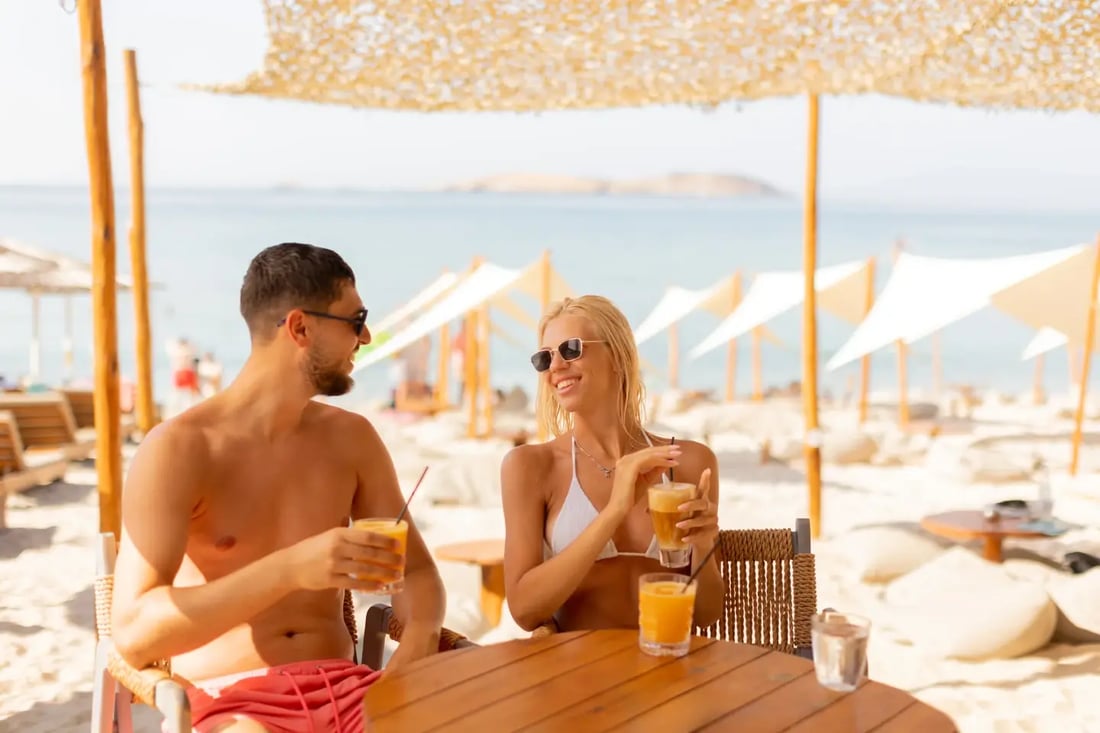 Couple sharing drinks at a beach club in Dubai, relaxed and smiling under umbrellas