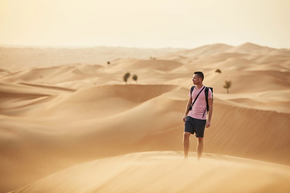 Traveller walking across red sand dunes in the UAE desert