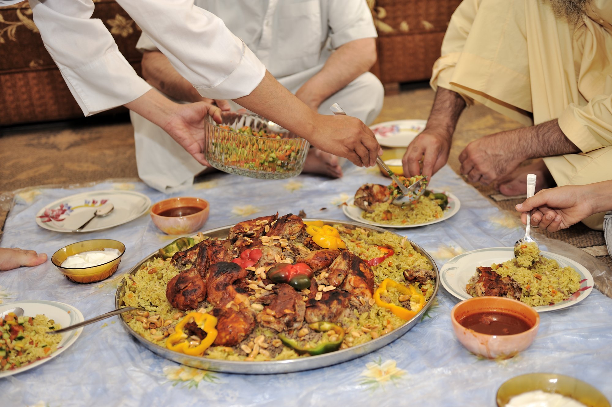 Hands reaching into a shared platter of kabsa served on the floor, Saudi style