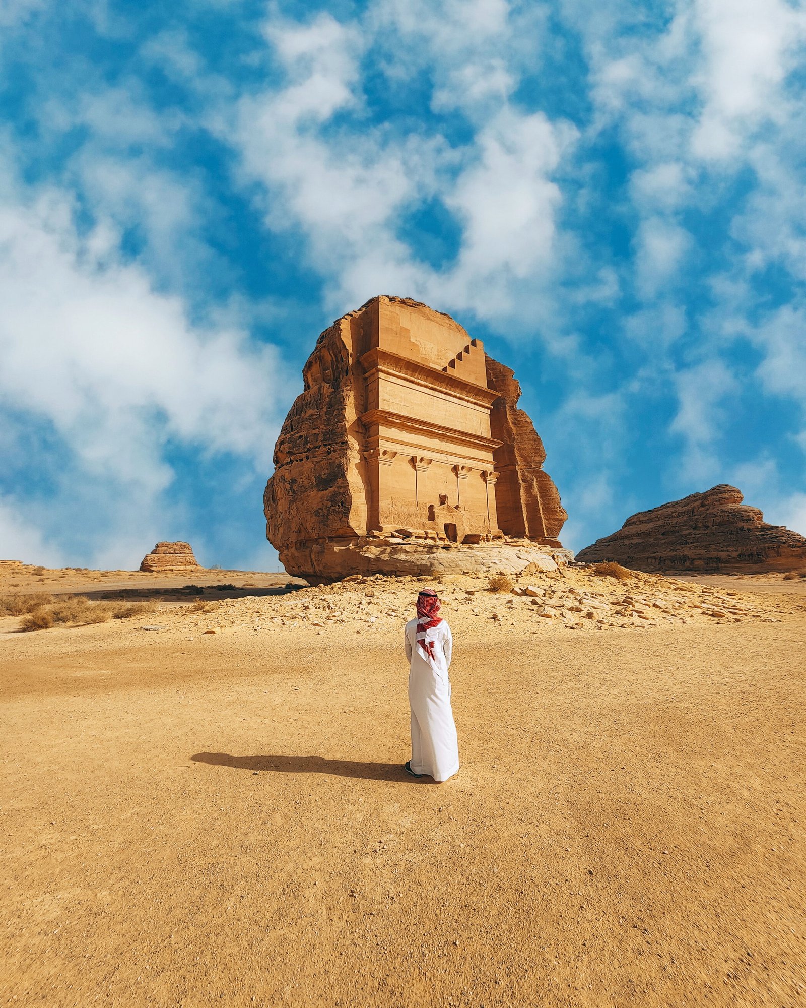 Man in a white thobe standing before the Qasr al-Farid tomb at Hegra, AlUla