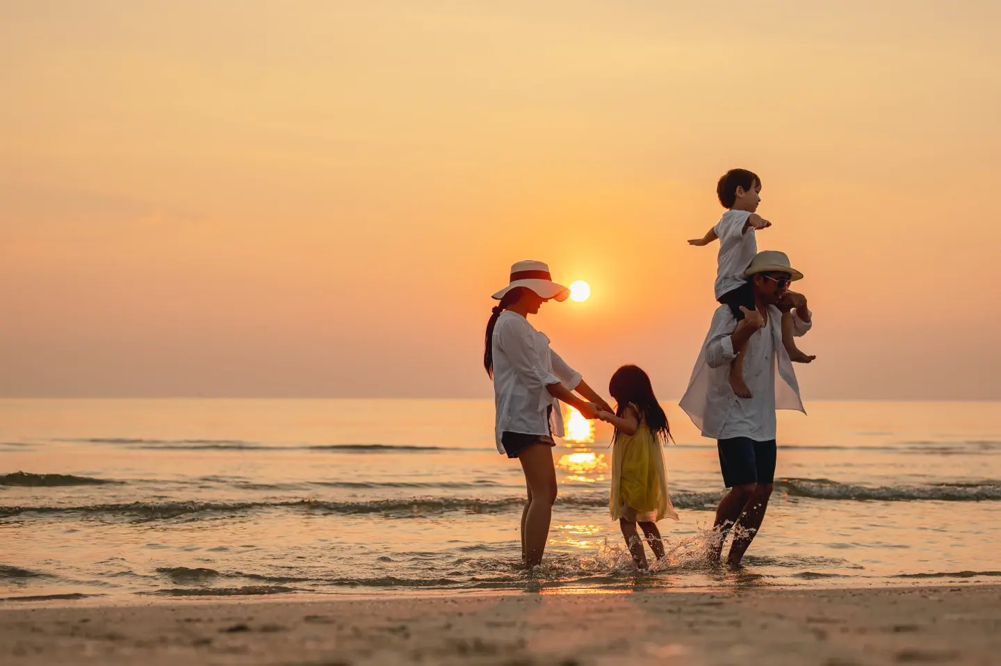 Family enjoying a sunset beach walk in Southeast Asia, wading through calm ocean water during a warm holiday evening.