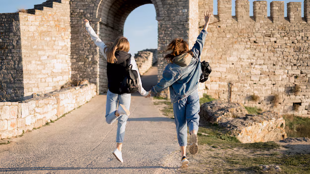 Two friends holding hands and jumping near a stone archway in the UK